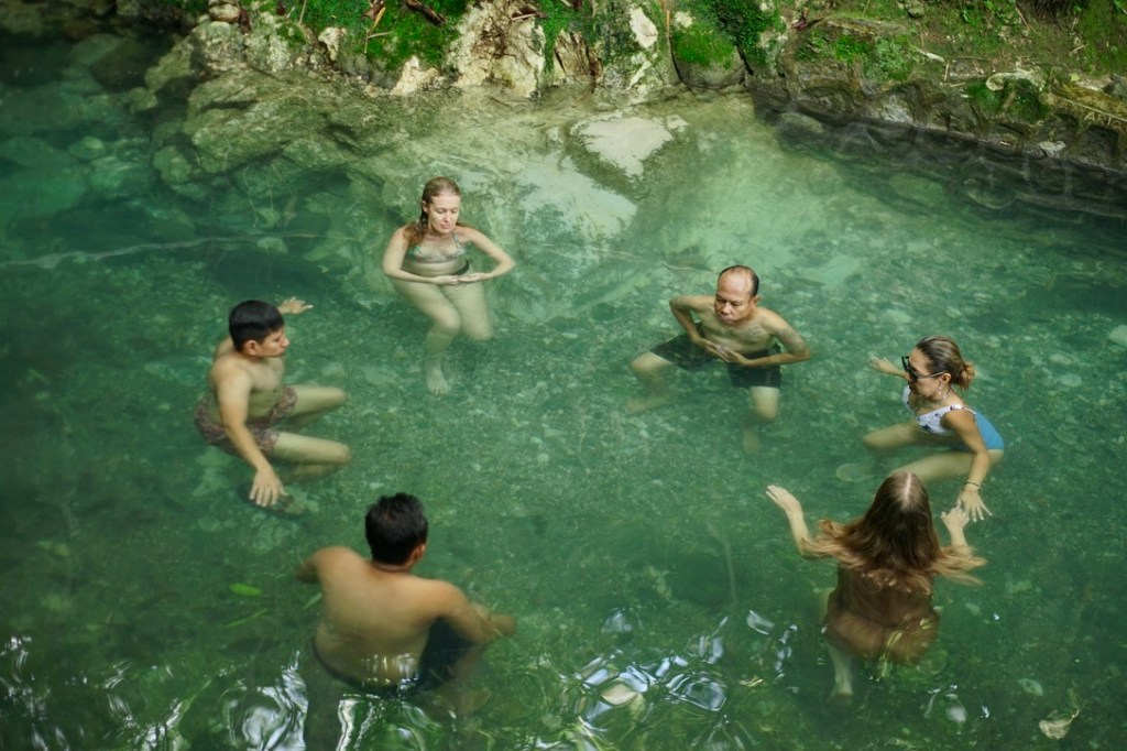People in a hot spring. The people are in clear, shallow water with light green tones.