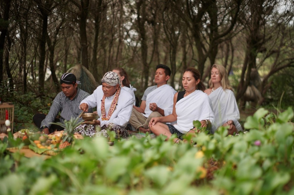 Three masked people sit with their backs against a boulder, in an outdoor setting with string lights and trees. Answer: Th...